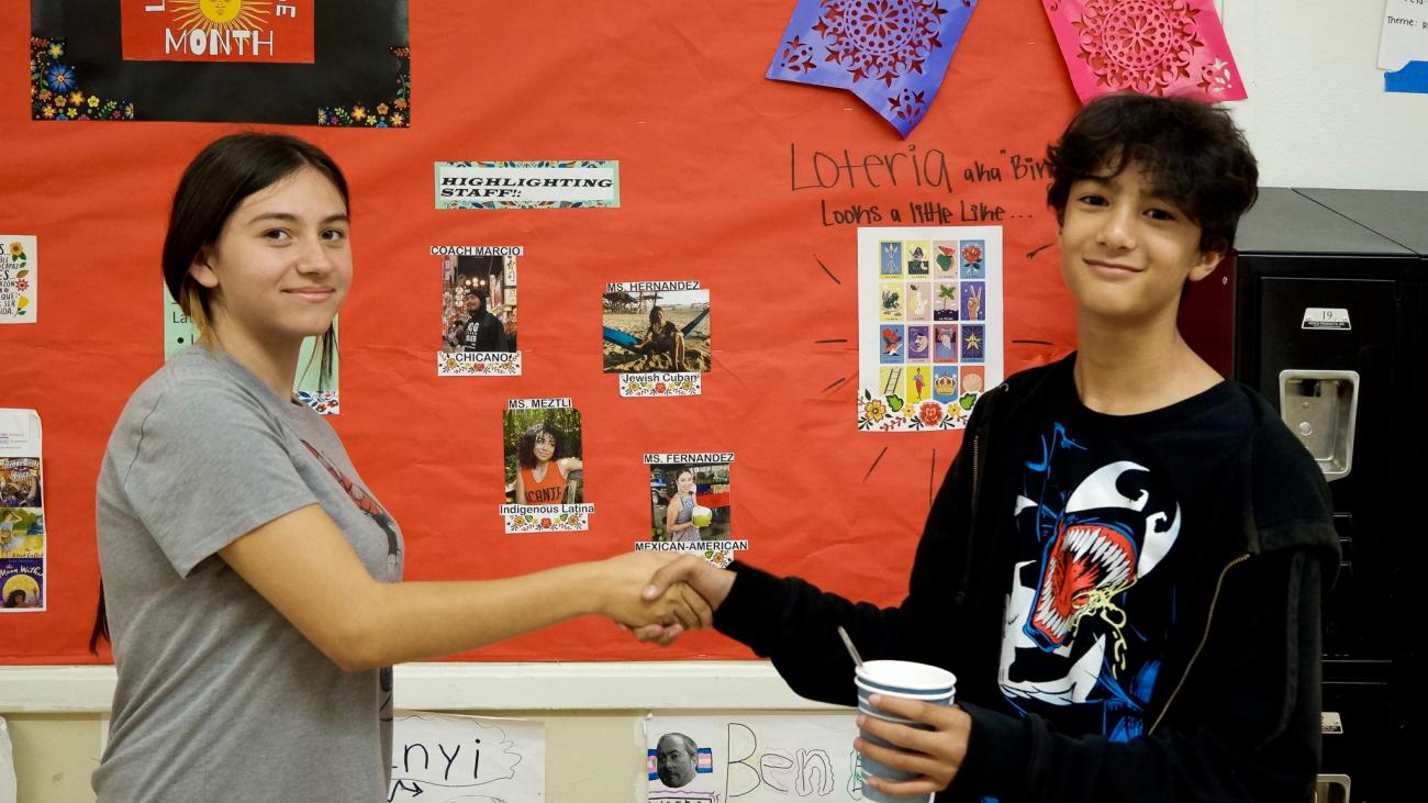 students shaking hands in front of a bulletin board