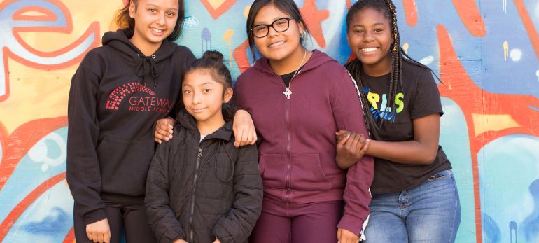 Middle school girls pose in front of a mural